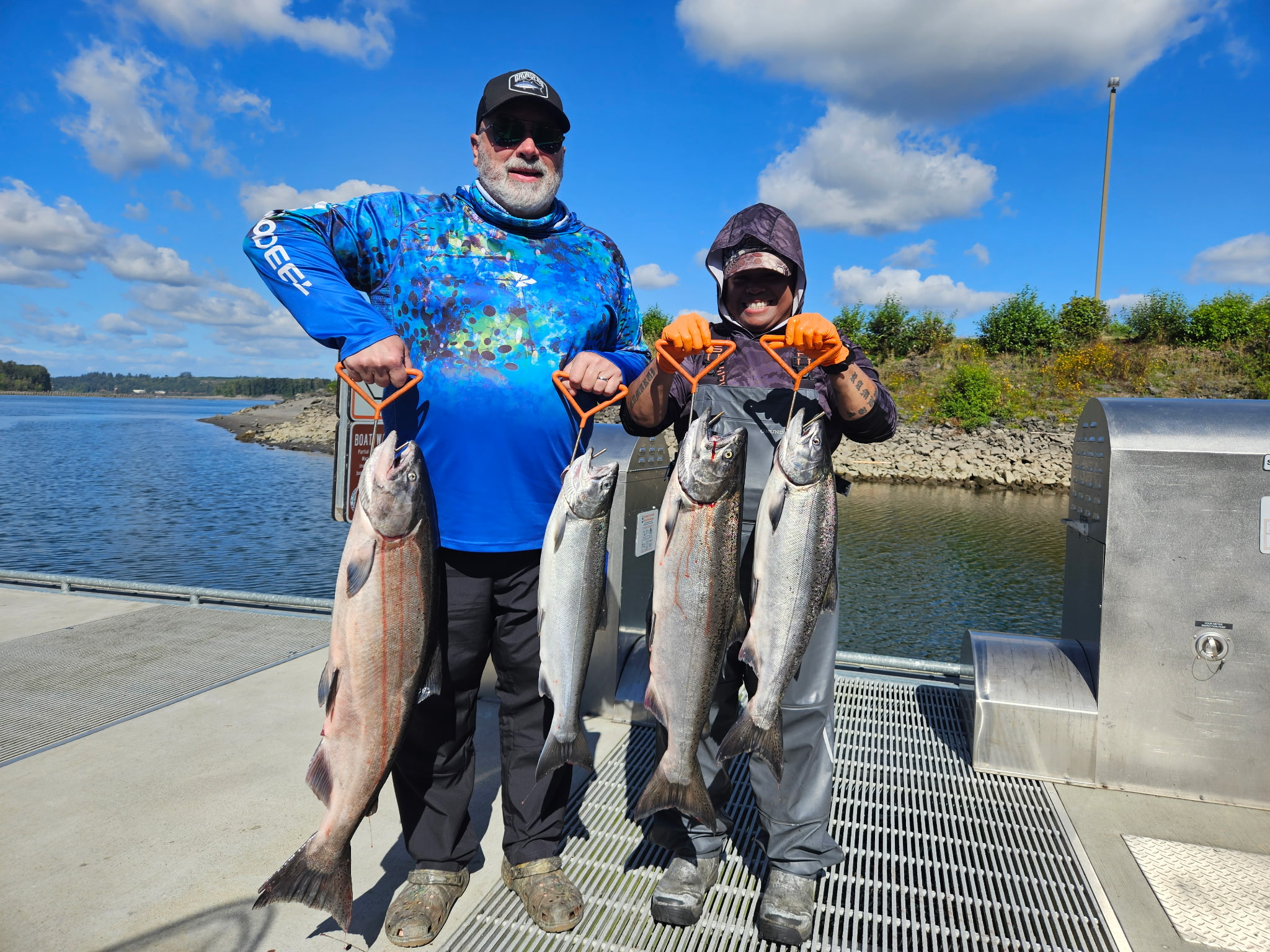 Two anglers, one in a fishing hoodie, holding four bright Chinook salmon on Tony's boat on a sunny Columbia River day.