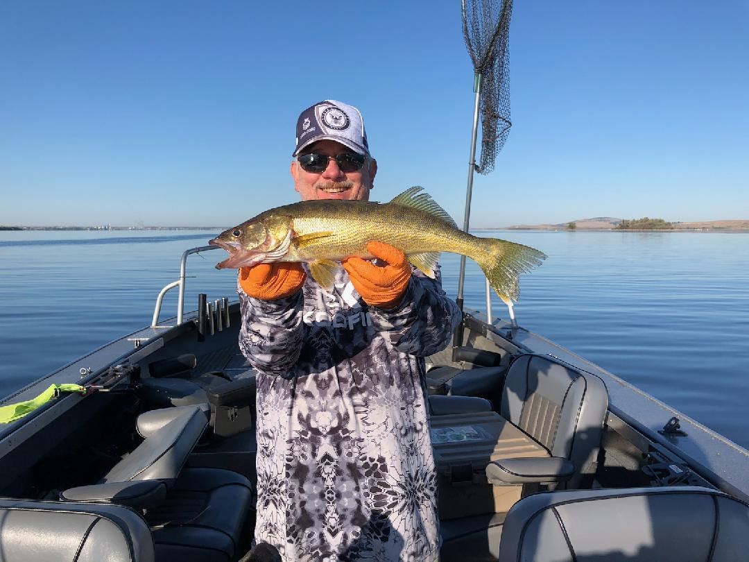 Tony Owsian on his guided fishing boat holding a walleye, Navy retired ball cap, glass-flat Columbia River behind.
