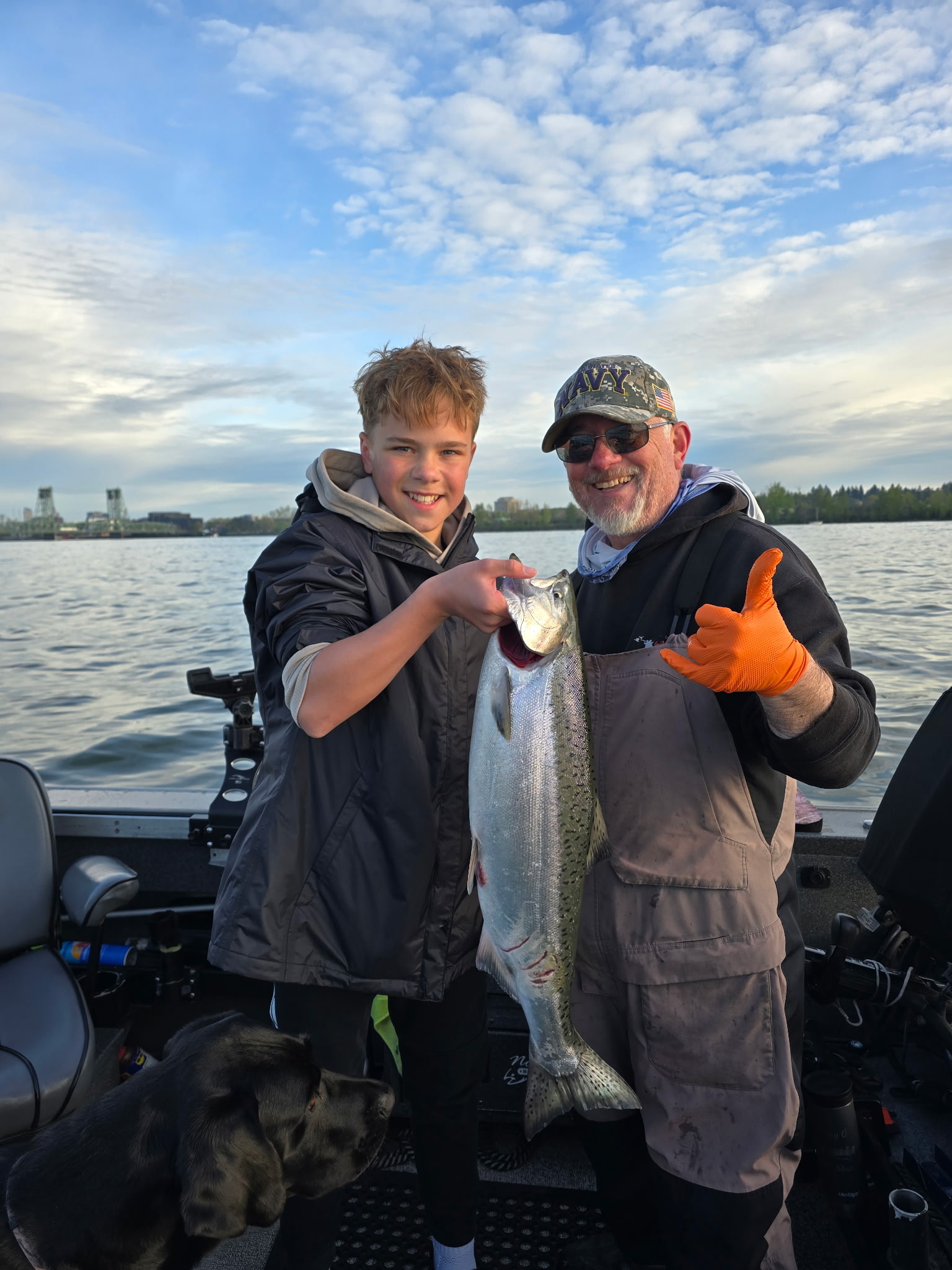Tony Owsian on his boat with a teenage angler holding a Chinook salmon at dusk, dog visible at the stern.